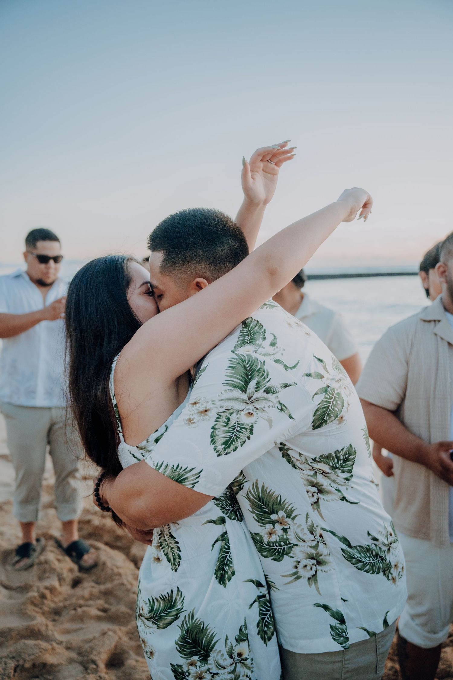 Celebratory embrace on beach during sunset with onlookers in background.