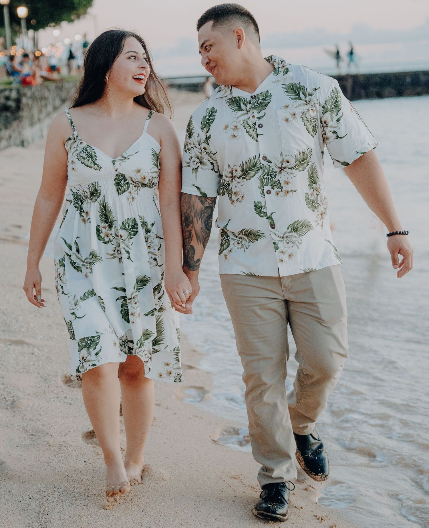 A couple in matching floral outfits walking hand in hand on a beach at sunset.