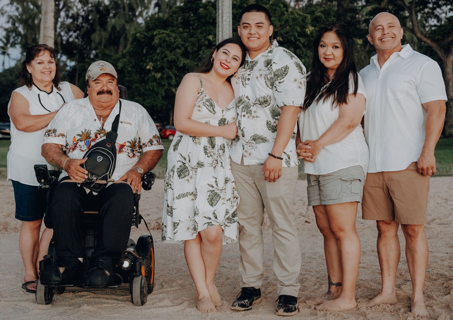 Family group photo on the beach wearing coordinated white and floral outfits.