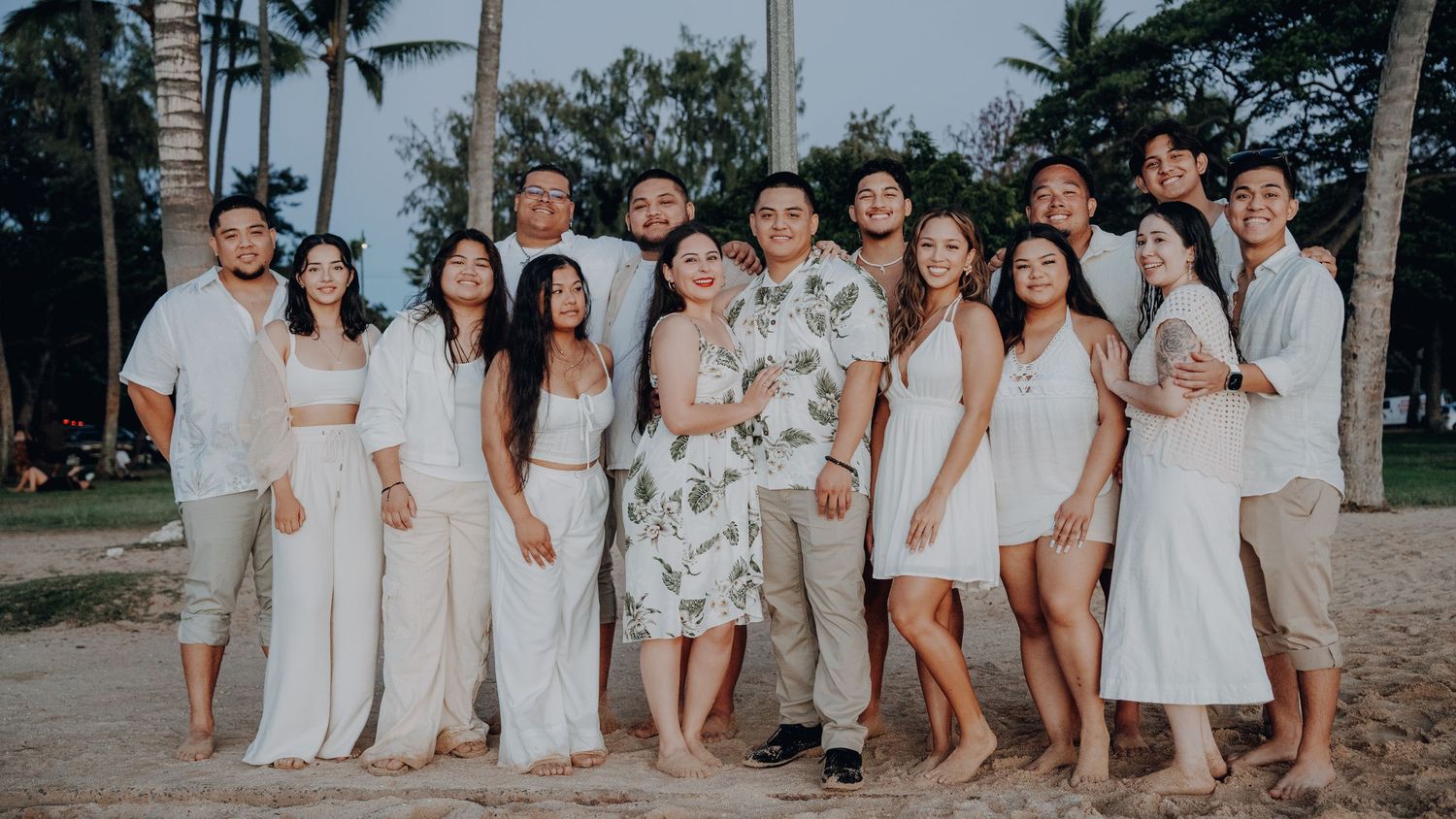 Wedding party in white attire poses together on a tropical beach with palm trees.