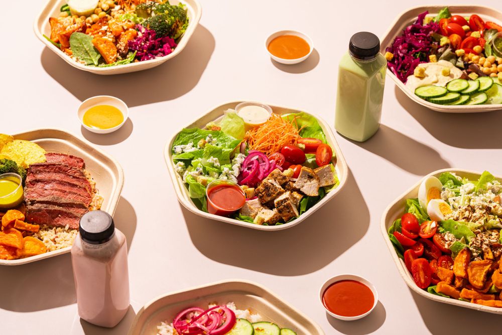 Colorful array of healthy lunch bowls with sauces and smoothies on white background.