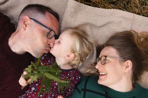Family lying on blanket outdoors sharing playful moment together in warm sunlight.