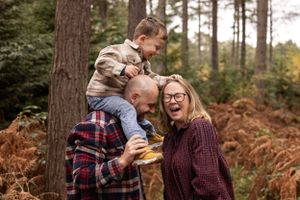 Candid family moment in autumn forest with laughter and joy among pine trees and ferns.