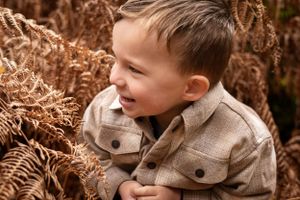 Child laughing while surrounded by golden autumn ferns in natural lighting.
