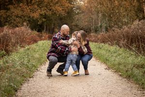 Family sharing playful moment together on dirt path surrounded by autumn foliage.