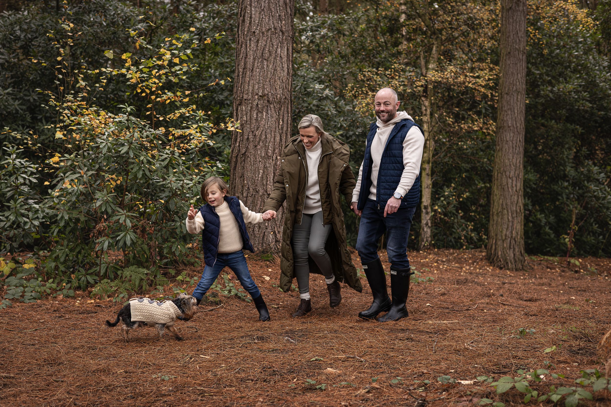 Family walking together with their small dog on a forest trail during autumn.