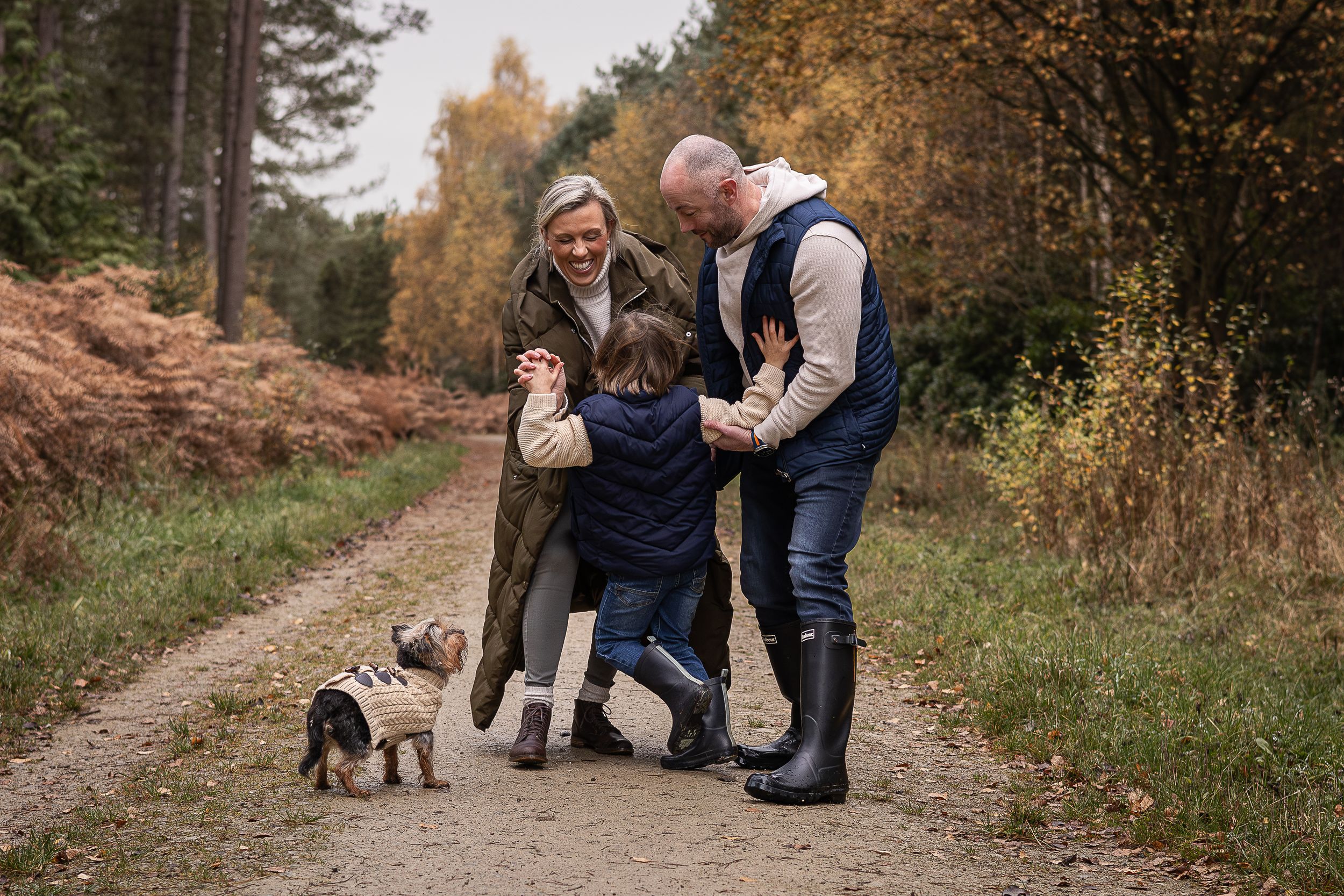 Family gathering with small dog on a countryside path during autumn.