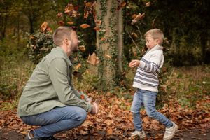 Parent and child play together in fallen autumn leaves.