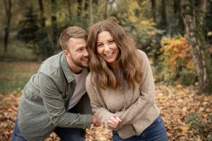 Couple laughs together among fallen autumn leaves in park setting.