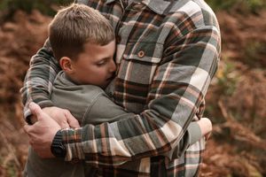 Tender embrace between a person in a plaid flannel shirt and another wearing grey outdoors.