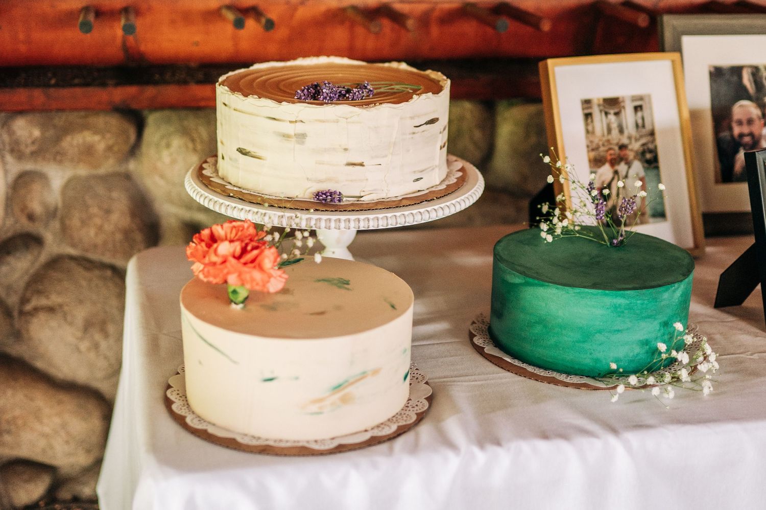 A series of rustic wedding cakes with textured buttercream frosting and floral decorations displayed at a reception venue.