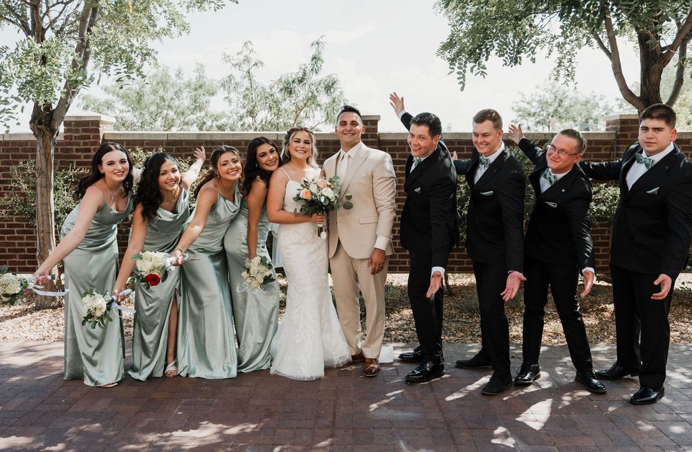 Wedding party poses outdoors in formal attire with sage green bridesmaid dresses and black suits.