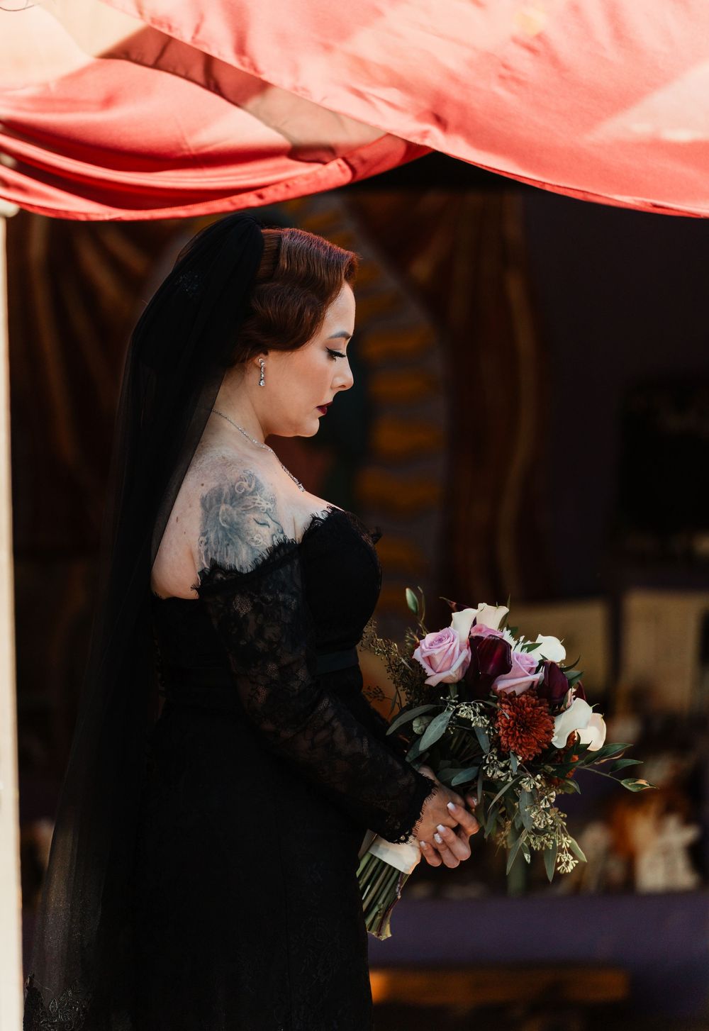 A romantic bridal portrait under a pink canopy featuring a black gothic wedding dress and floral bouquet.