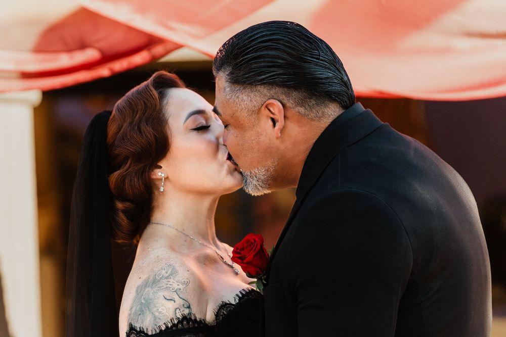 A couple in black attire share an intimate dance moment under warm lighting at an event.