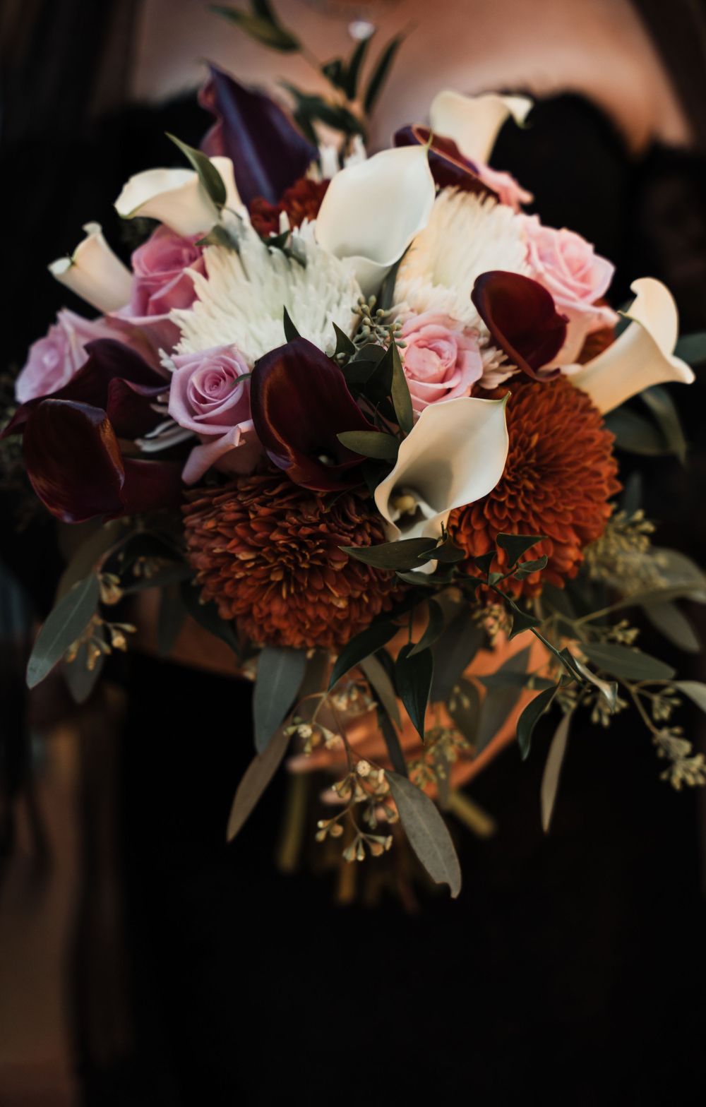 Close-up of a moody fall wedding bouquet with burgundy dahlias, calla lilies, and pink roses.