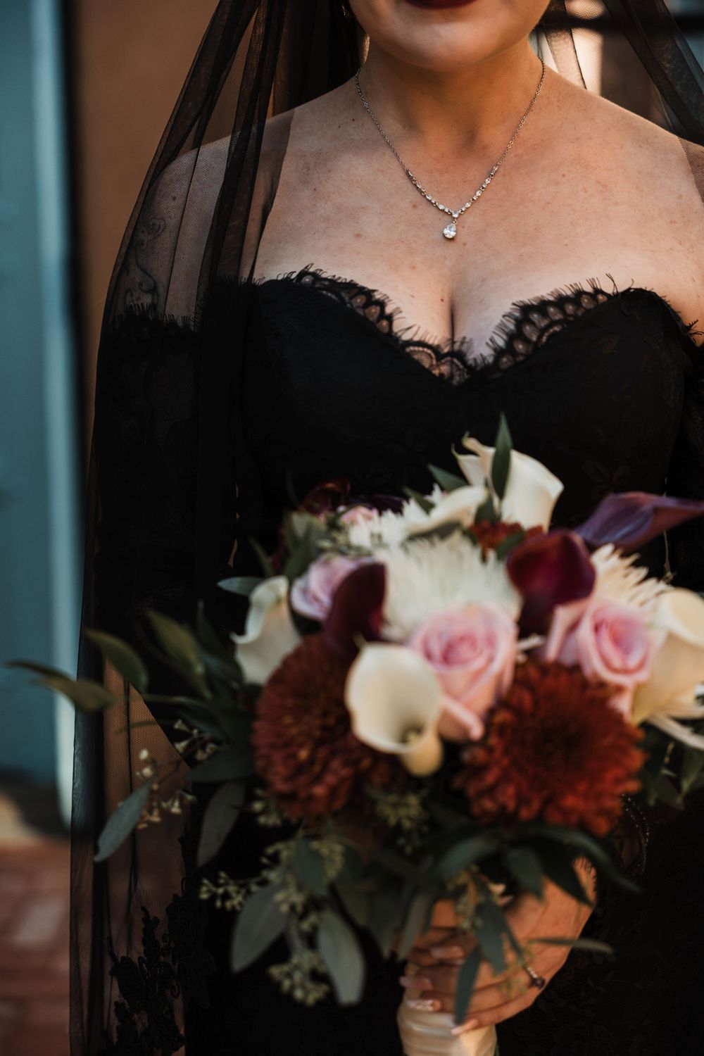 Close-up details of black lace wedding dress bodice with pink and burgundy floral bouquet.