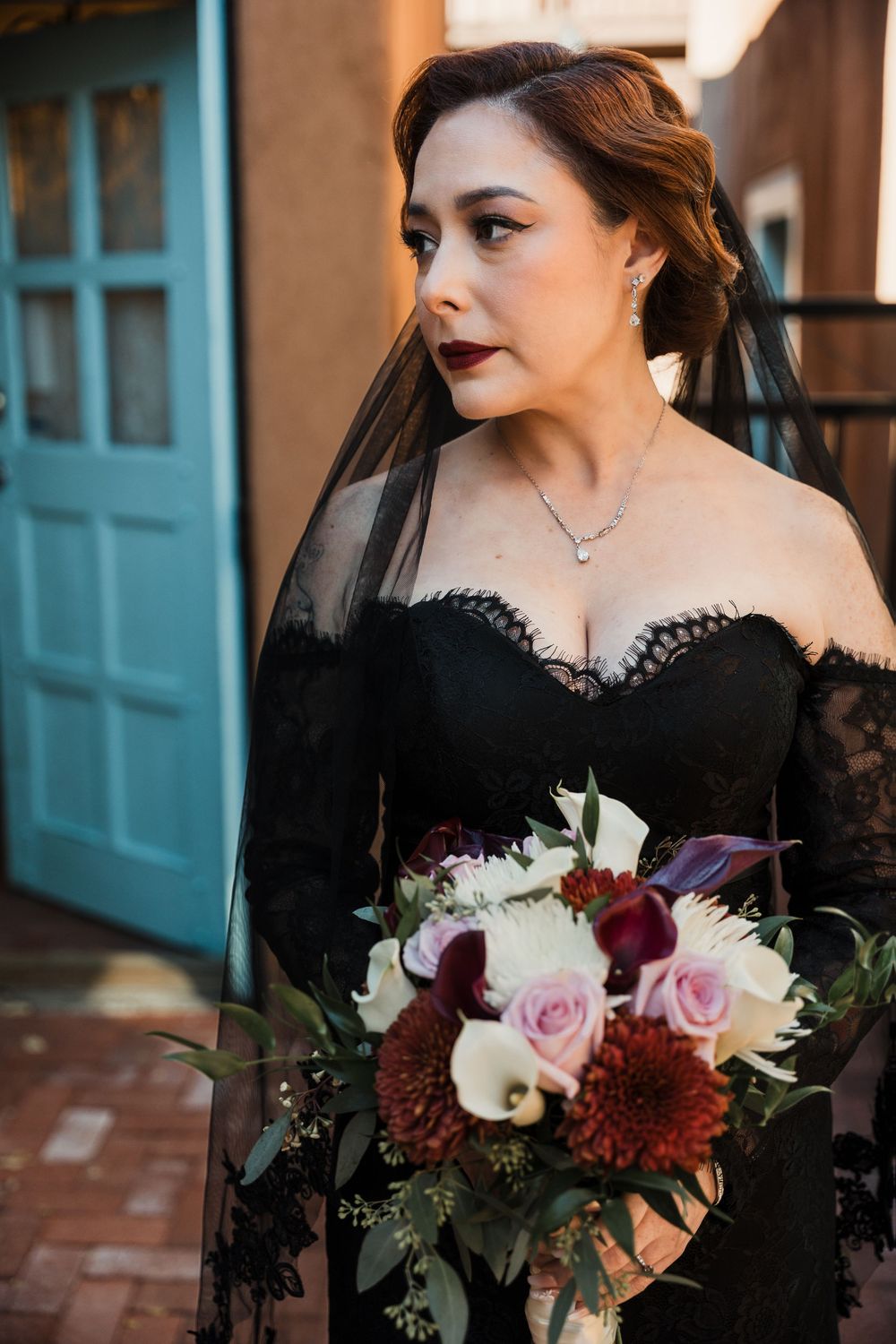 A wedding bouquet with burgundy dahlias, white calla lilies, and pink roses held against a black lace dress.
