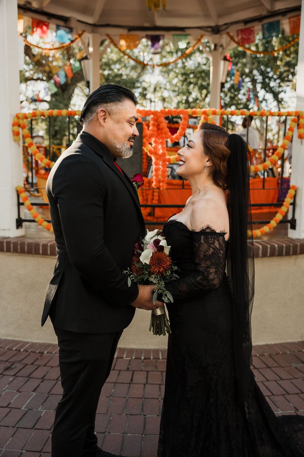 A couple in black formal attire share a romantic moment together in a decorated outdoor venue.