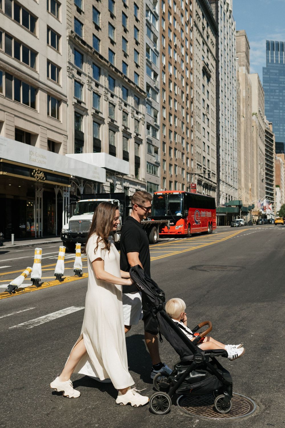 Family walking down a city street in New York with tall buildings and a red bus in the background.