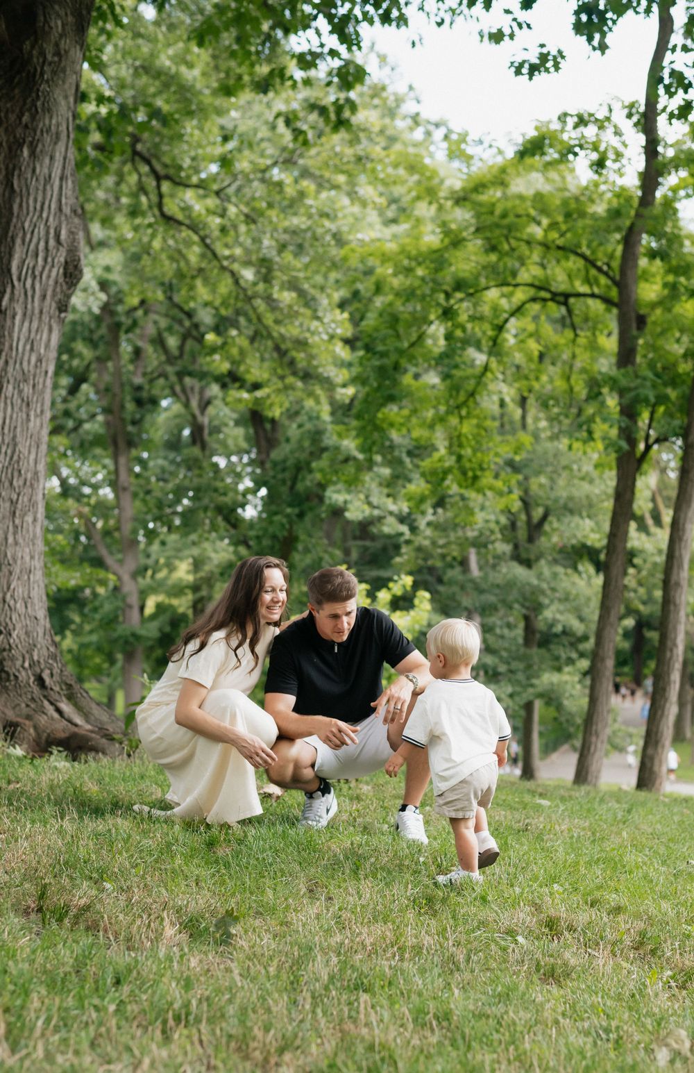 A family plays together on a grassy hill in a lush park setting.