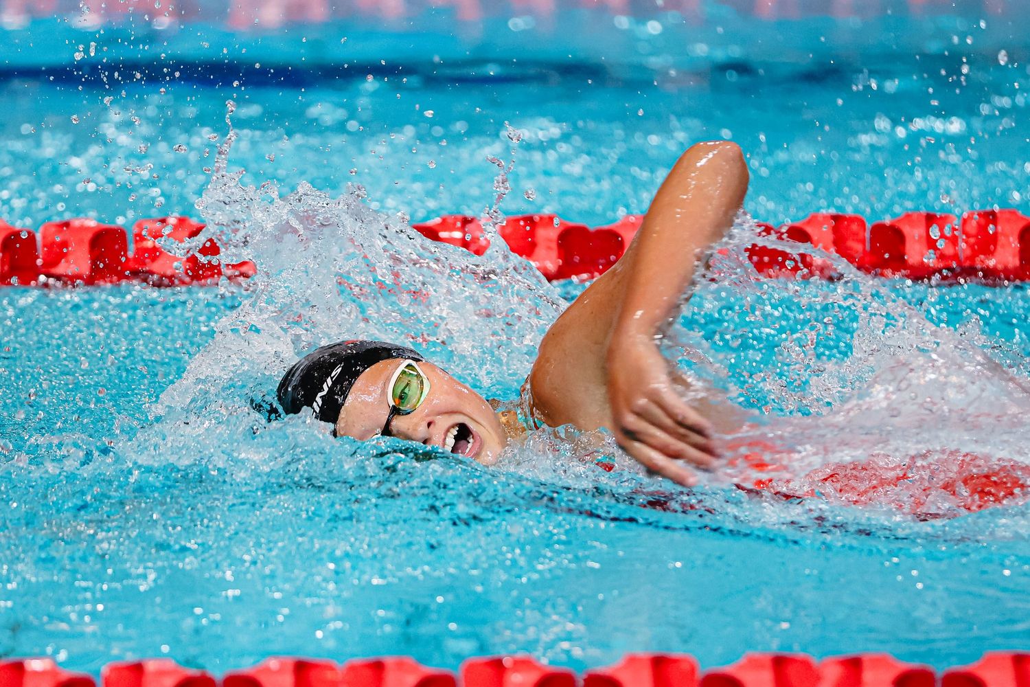 Swimmer performing freestyle stroke in bright blue pool water during competitive race.