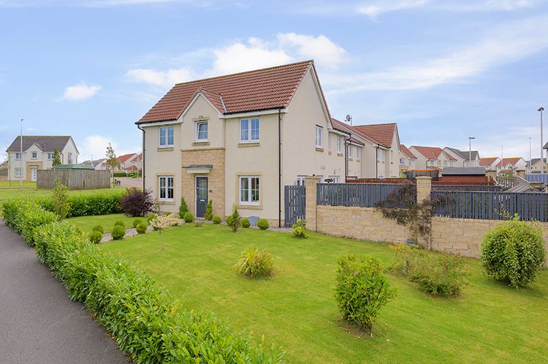 Panoramic view of modern suburban houses with well-maintained green lawns and landscaping under blue skies.