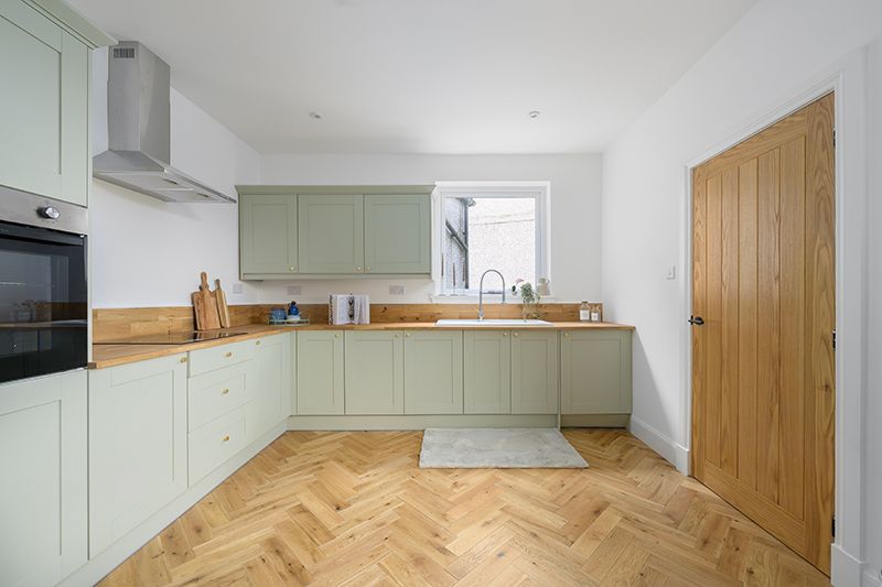 Modern kitchen interior with sage green cabinets, herringbone wood flooring and stainless steel appliances.