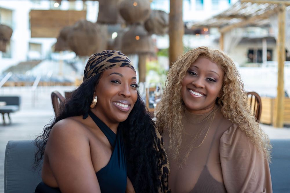 Three smiling friends pose together outdoors while enjoying a sunny day at a beachside location.