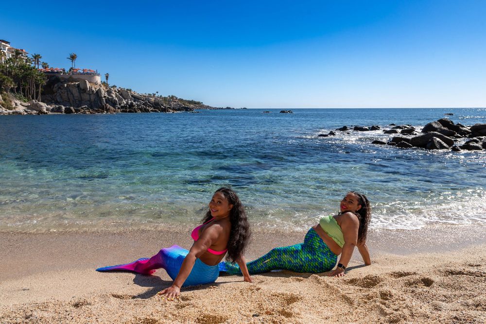 People relaxing and enjoying a sunny day at a beautiful tropical beach with crystal clear blue waters and rocky coastline.
