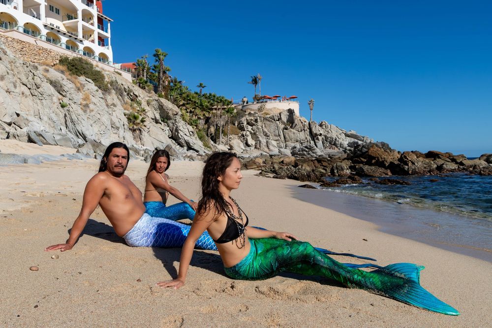 Coastal resort hotel with white balconies overlooks a pristine beach and turquoise ocean waters on a sunny day.