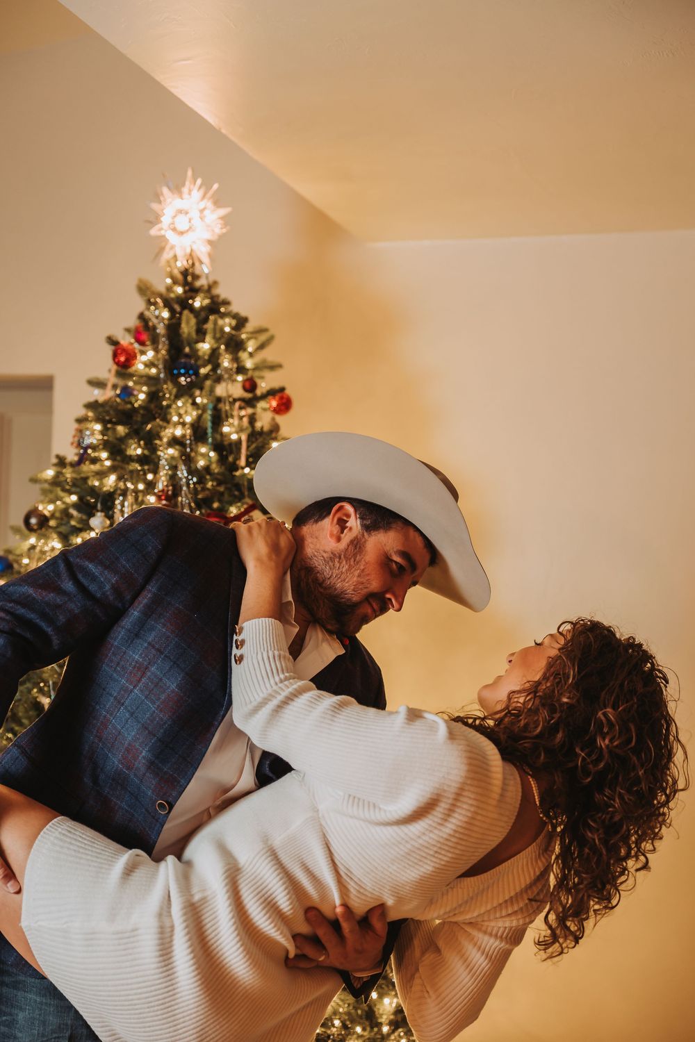 A romantic holiday moment with a couple dancing in front of a decorated Christmas tree with glowing lights.