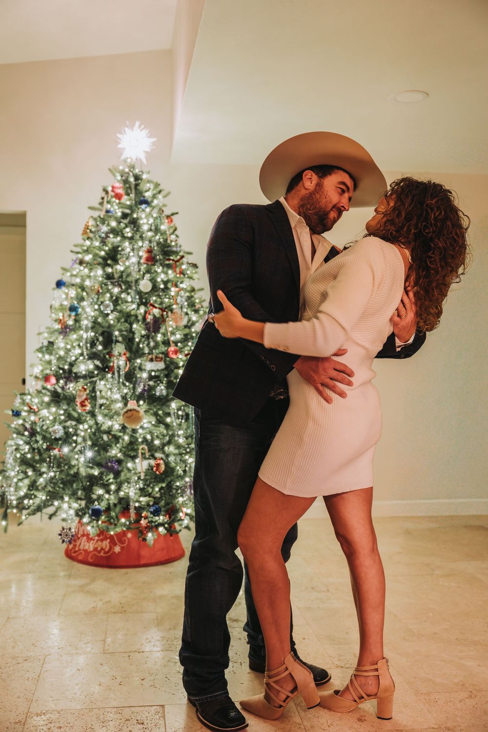 A couple dances romantically in front of a lit Christmas tree in a series of candid dance move photos.