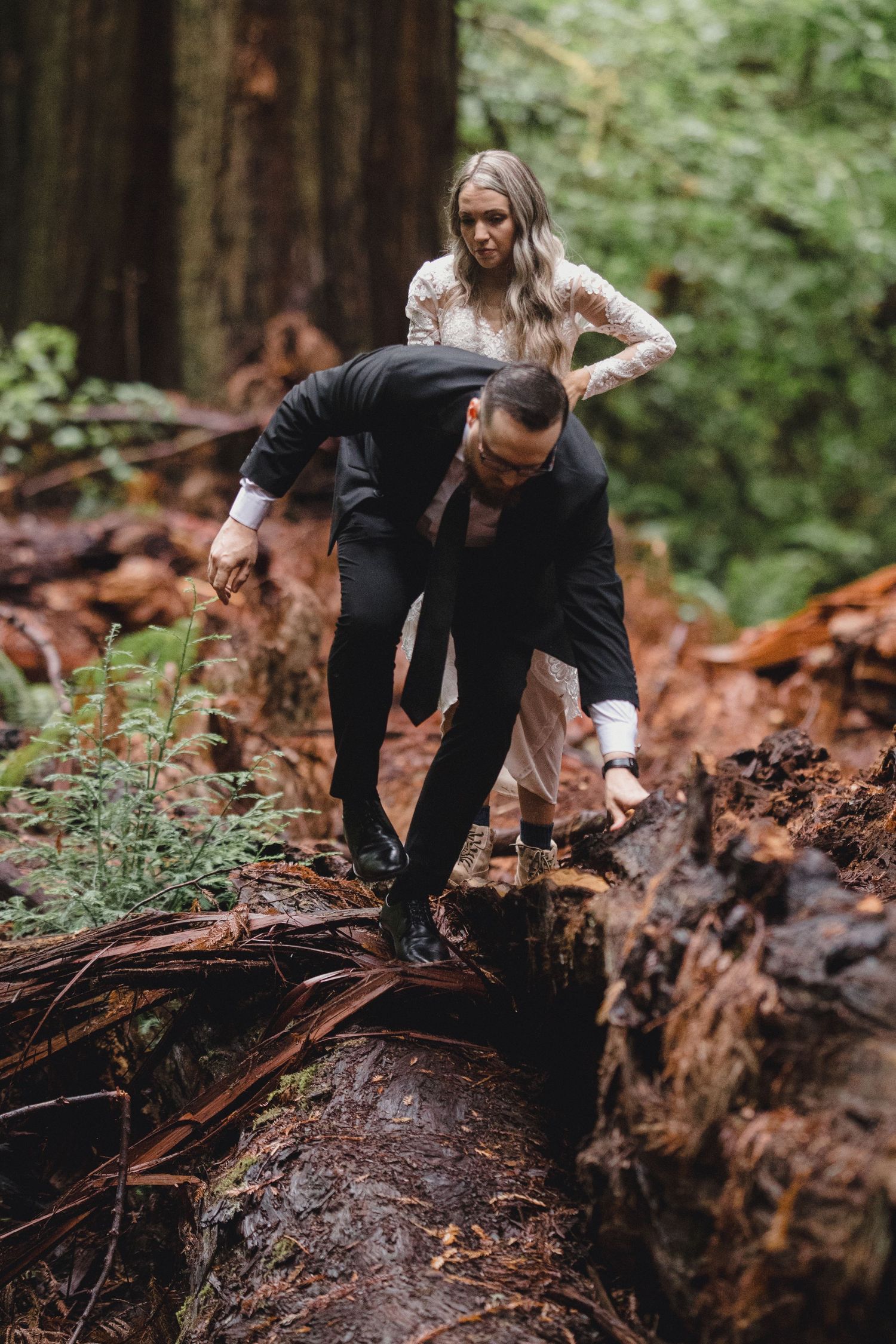 A person in dark clothing explores a fallen redwood tree trunk in a lush forest setting.