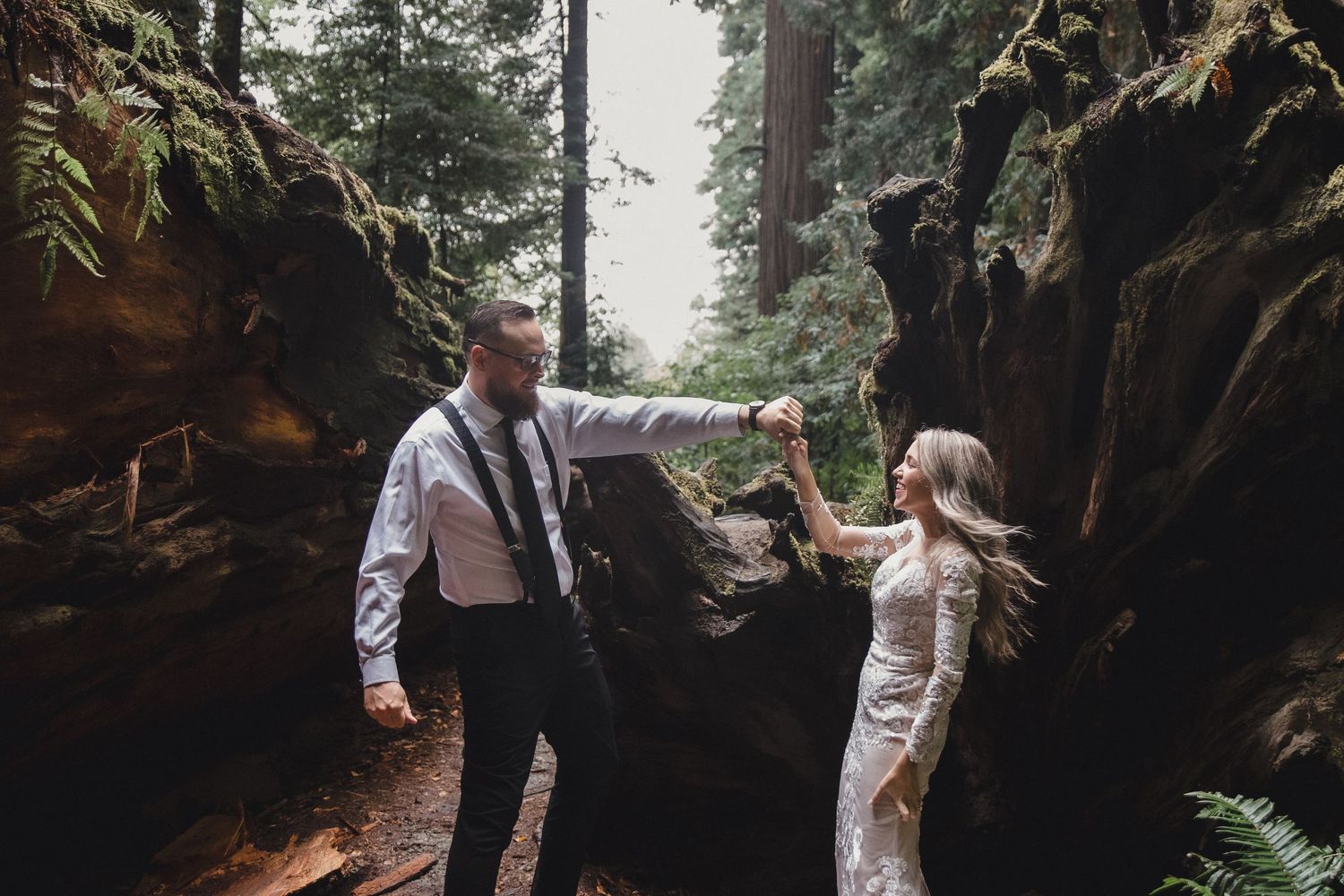 A couple walks through a misty forest path surrounded by tall evergreen trees and ferns in the Pacific Northwest.