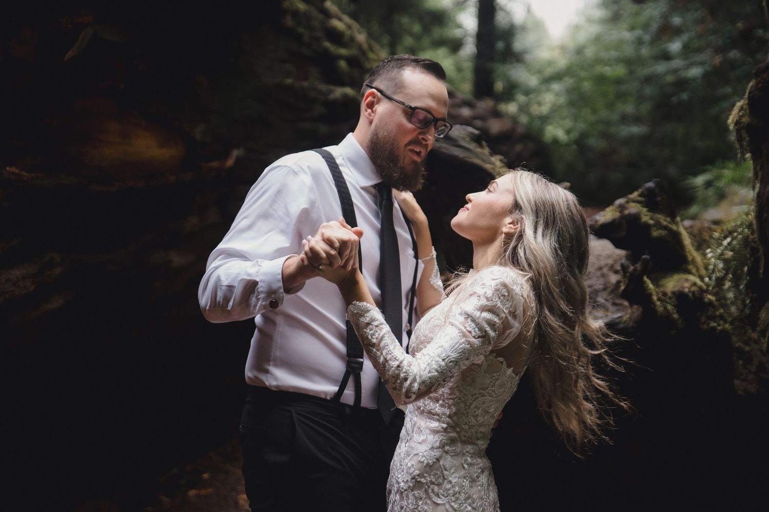 A couple in formal wedding attire share intimate moments in a romantic forest setting.