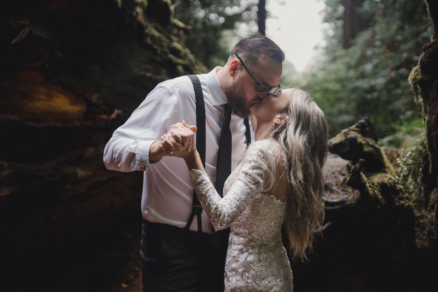 A couple in wedding attire shares intimate moments in a misty forest setting during their romantic photoshoot.
