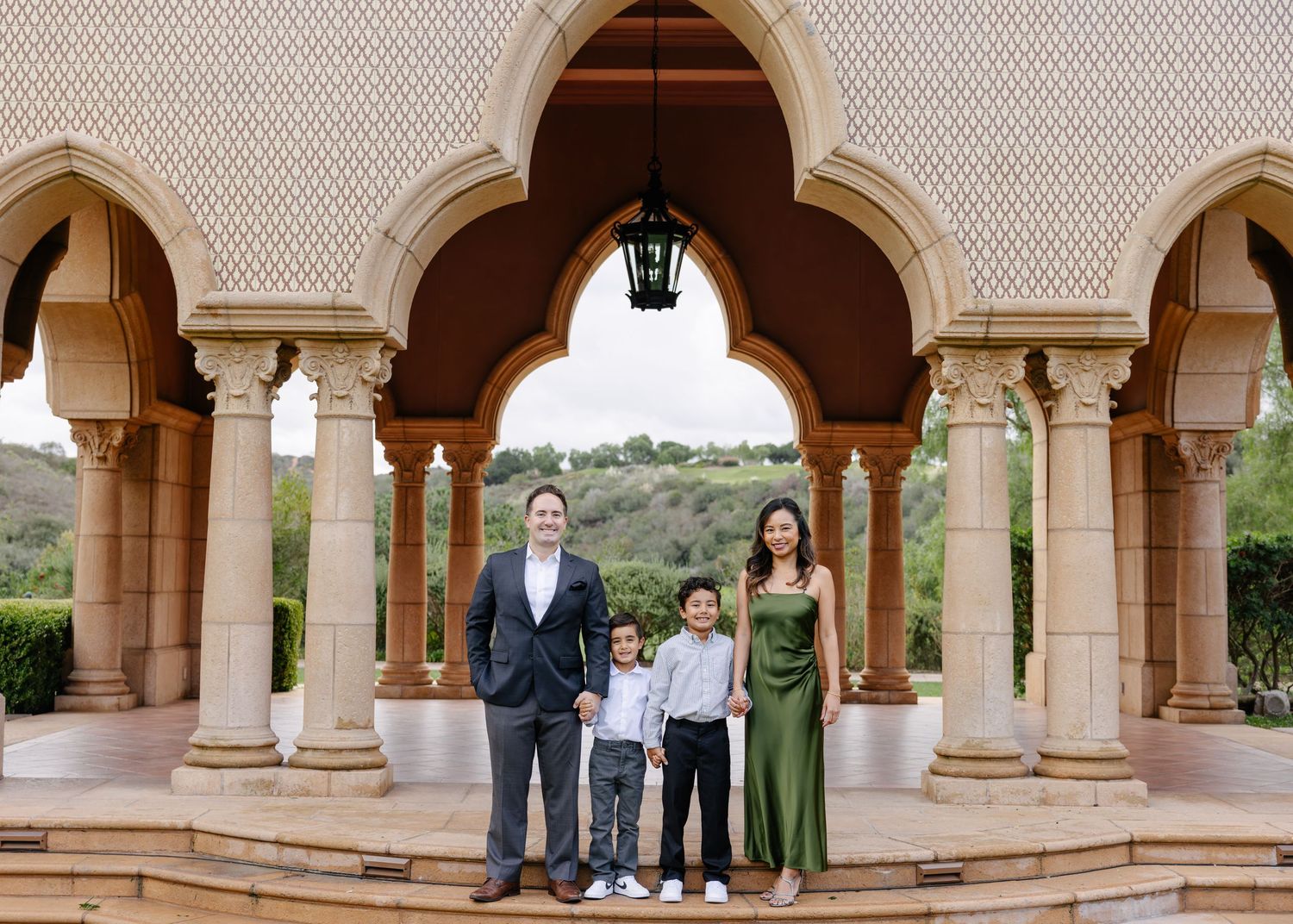 A family poses together under ornate stone arches at a Mediterranean-style building with columns and lanterns.