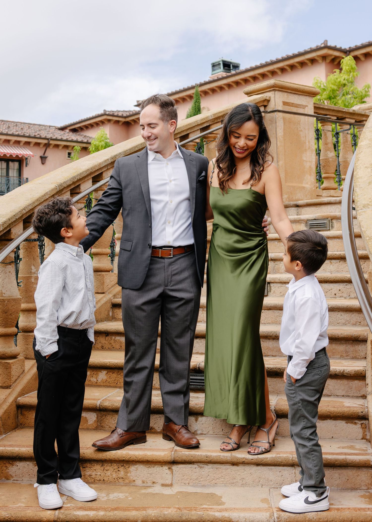 Family poses playfully on outdoor stone steps of a Spanish-style building.