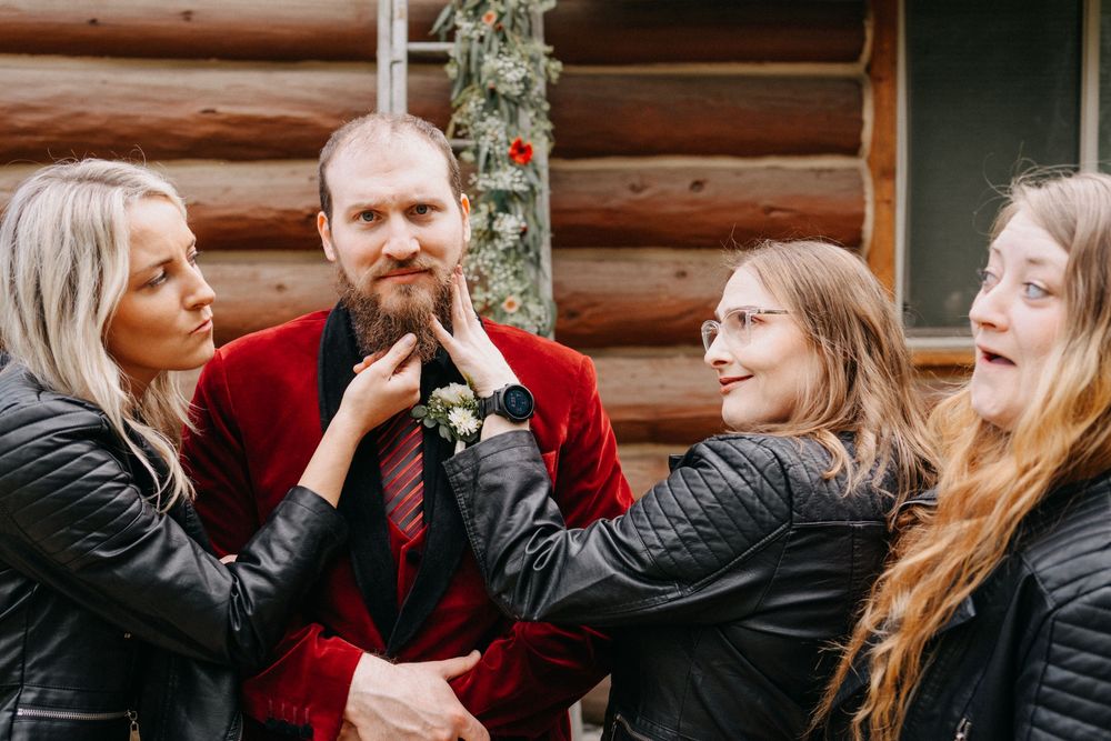 Wedding party members share intimate moments and laughter outside a rustic cabin.