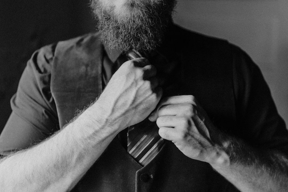 Close-up black and white photo of person adjusting tie and formal attire.