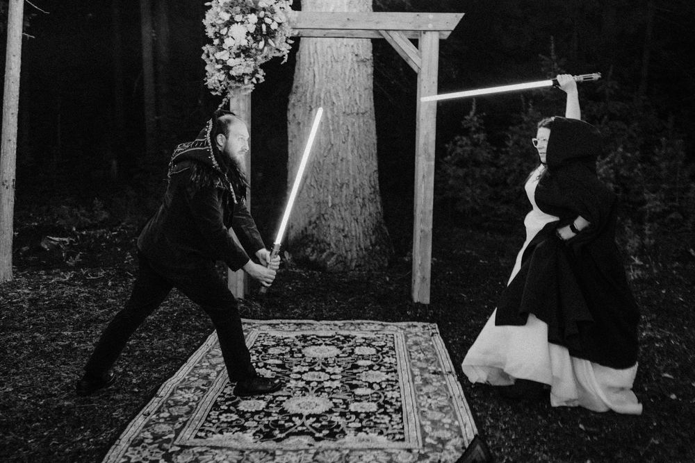 Dramatic black and white photo of couple sword fighting on decorative rug at wedding ceremony.