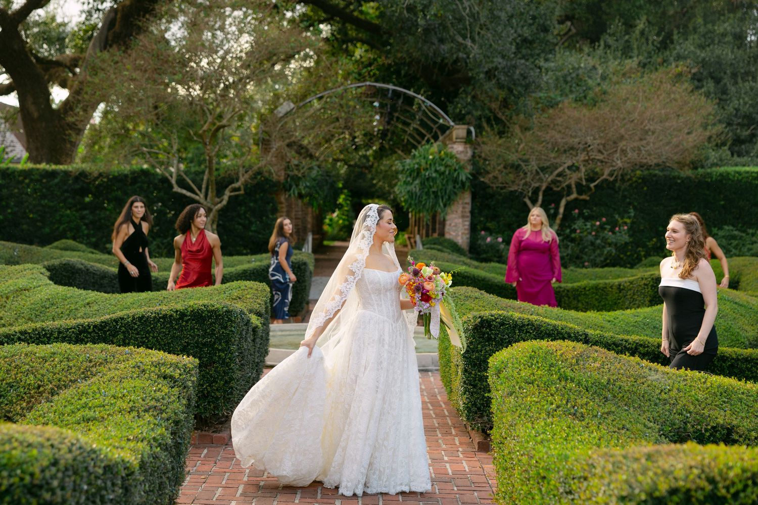 Wedding party walking through a lush garden pathway with manicured hedges and greenery. unique wedding photos. creative wedding photography