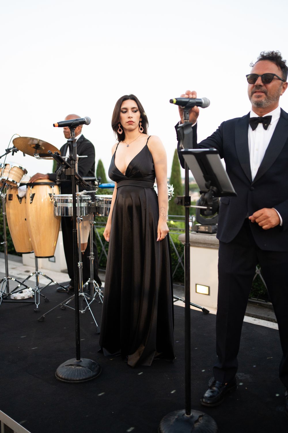 Musicians in formal black attire perform with percussion instruments at an outdoor event.