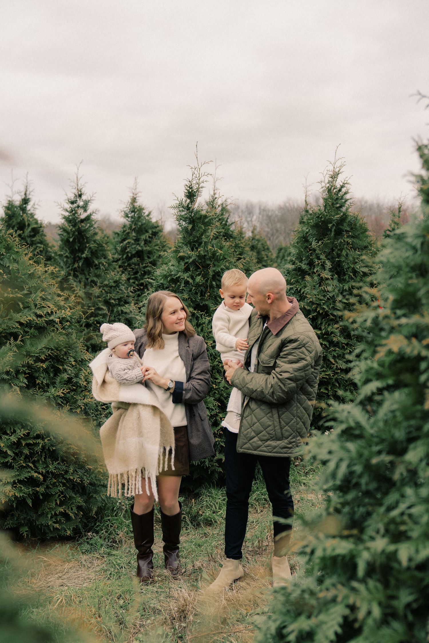 Family enjoying a winter day together at a Christmas tree farm among evergreen trees.