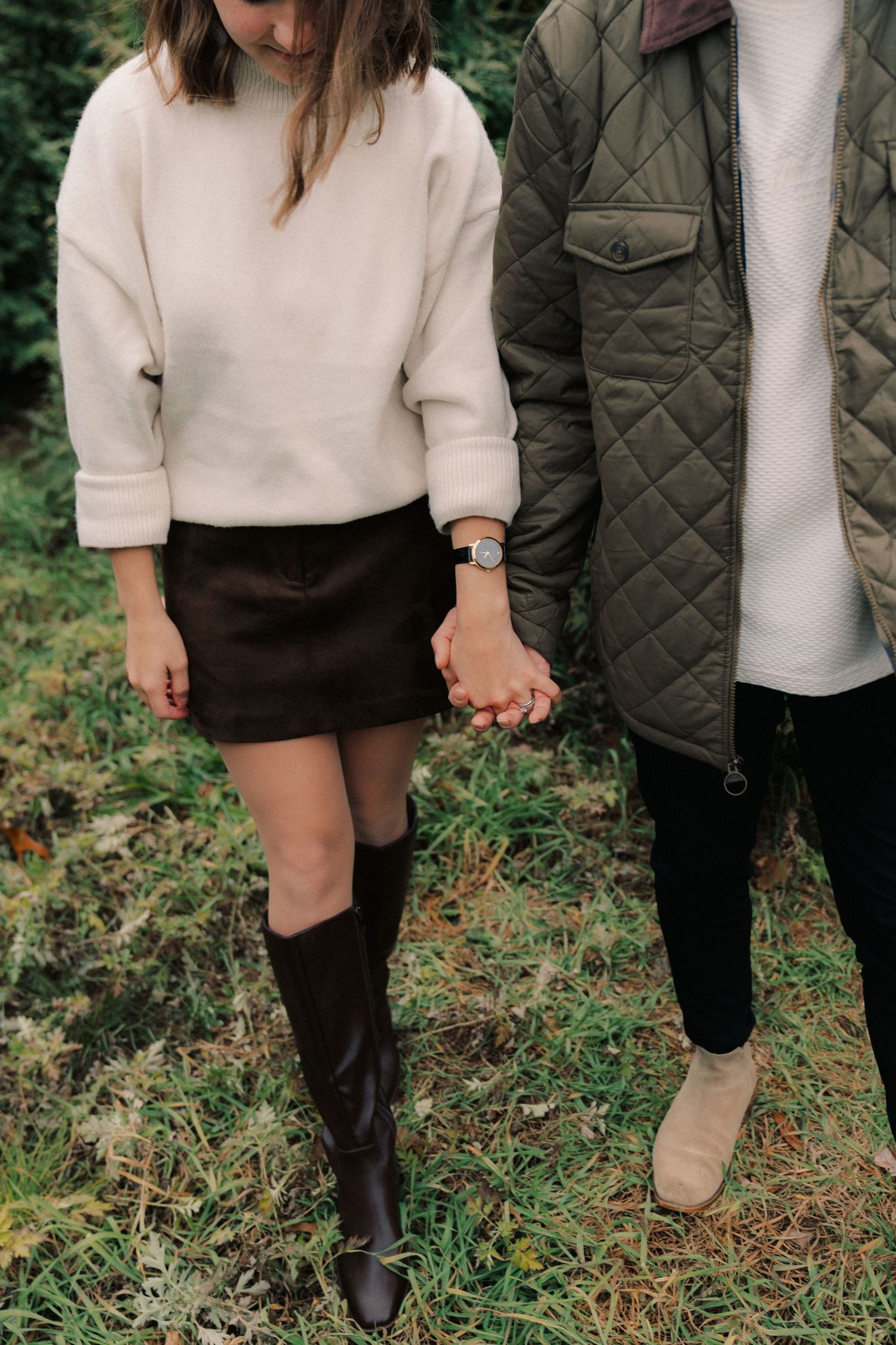 Close-up view of people holding hands while wearing fall attire including boots, quilted jacket and knit sweater.