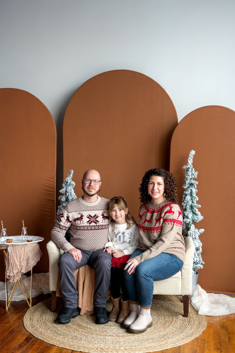 Family of three in Nordic Christmas sweaters sitting together on a bench with holiday decor.