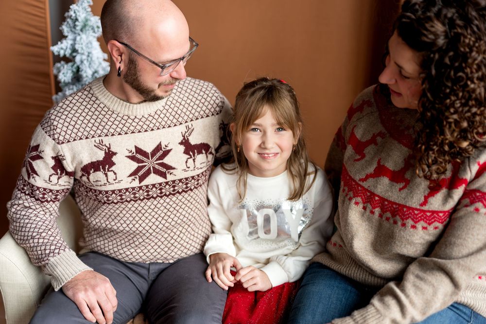 Smiling family in coordinating Christmas sweaters sharing a joyful moment on a cozy bench.