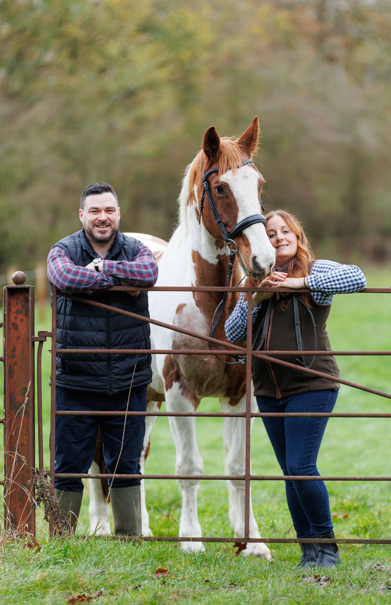 A brown horse and rider in a white sweater pose together against autumn foliage in soft natural lighting.