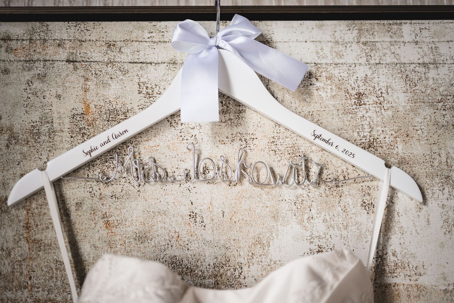 Multiple white wedding dresses displayed on hangers against a vintage wall.