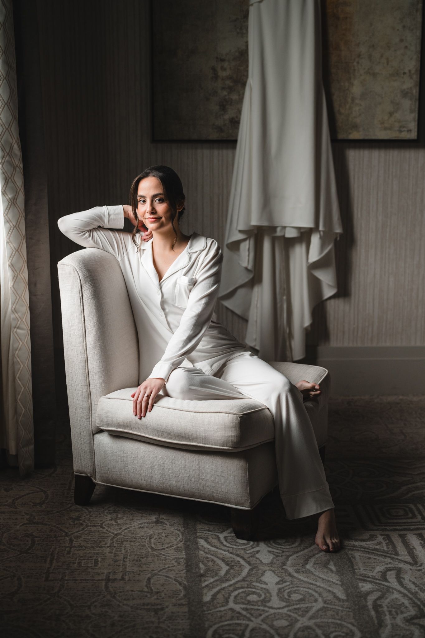 Elegant white lounge chair against a textured wall in a bridal suite.